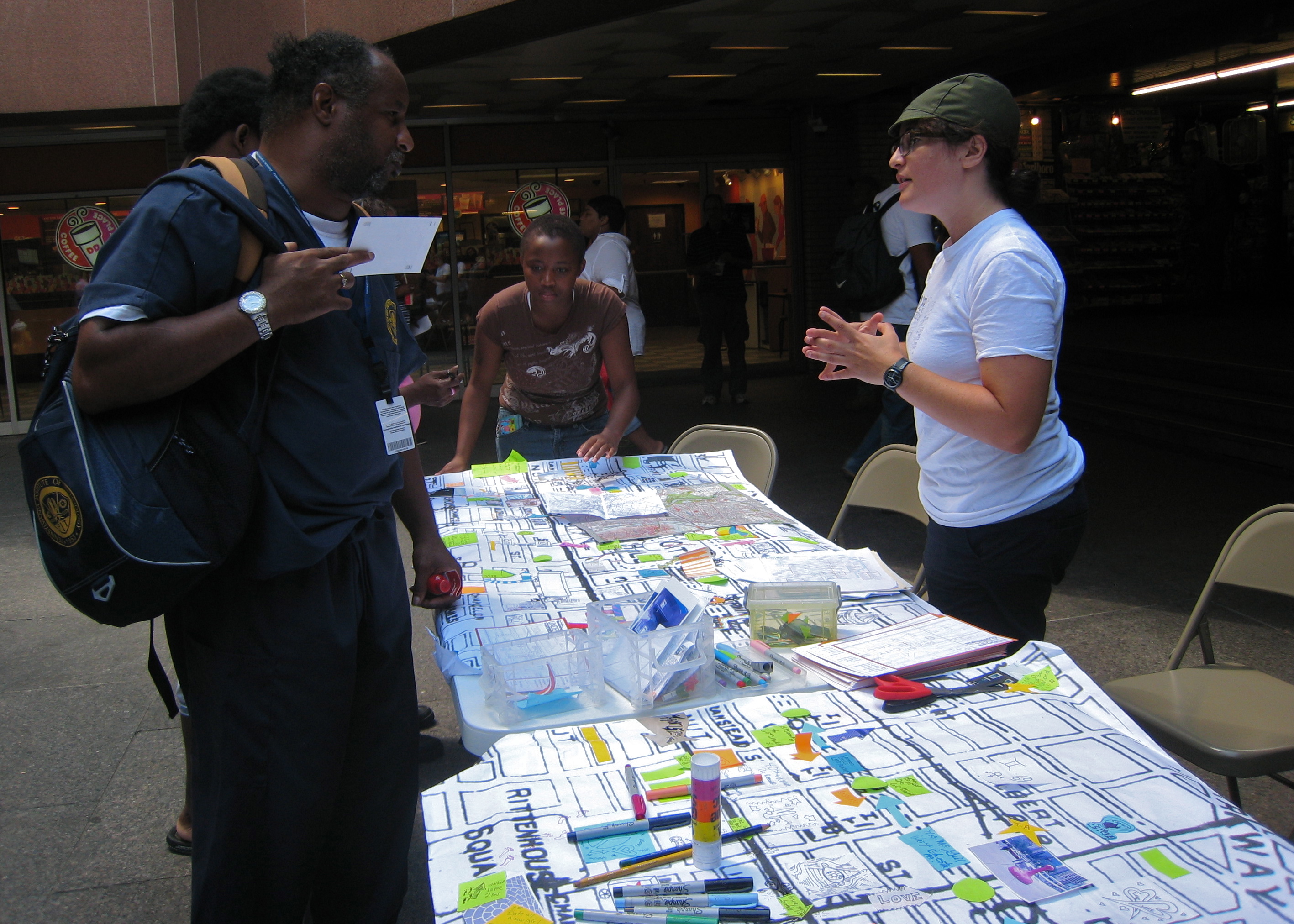 (Miriam Singer (right) talking to people passing through Centre Square's subway concourse entrance, asking them to add their routes and stories to the big map.)