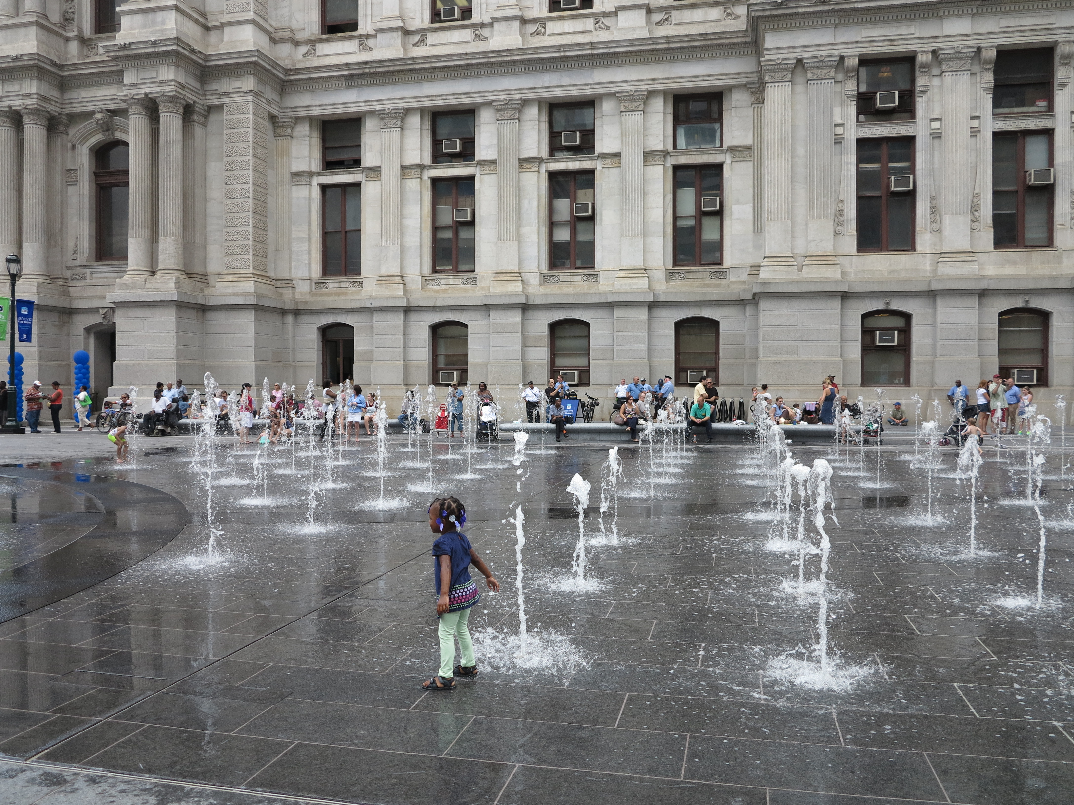 Kids splash in fountains while grown-ups watch from benches