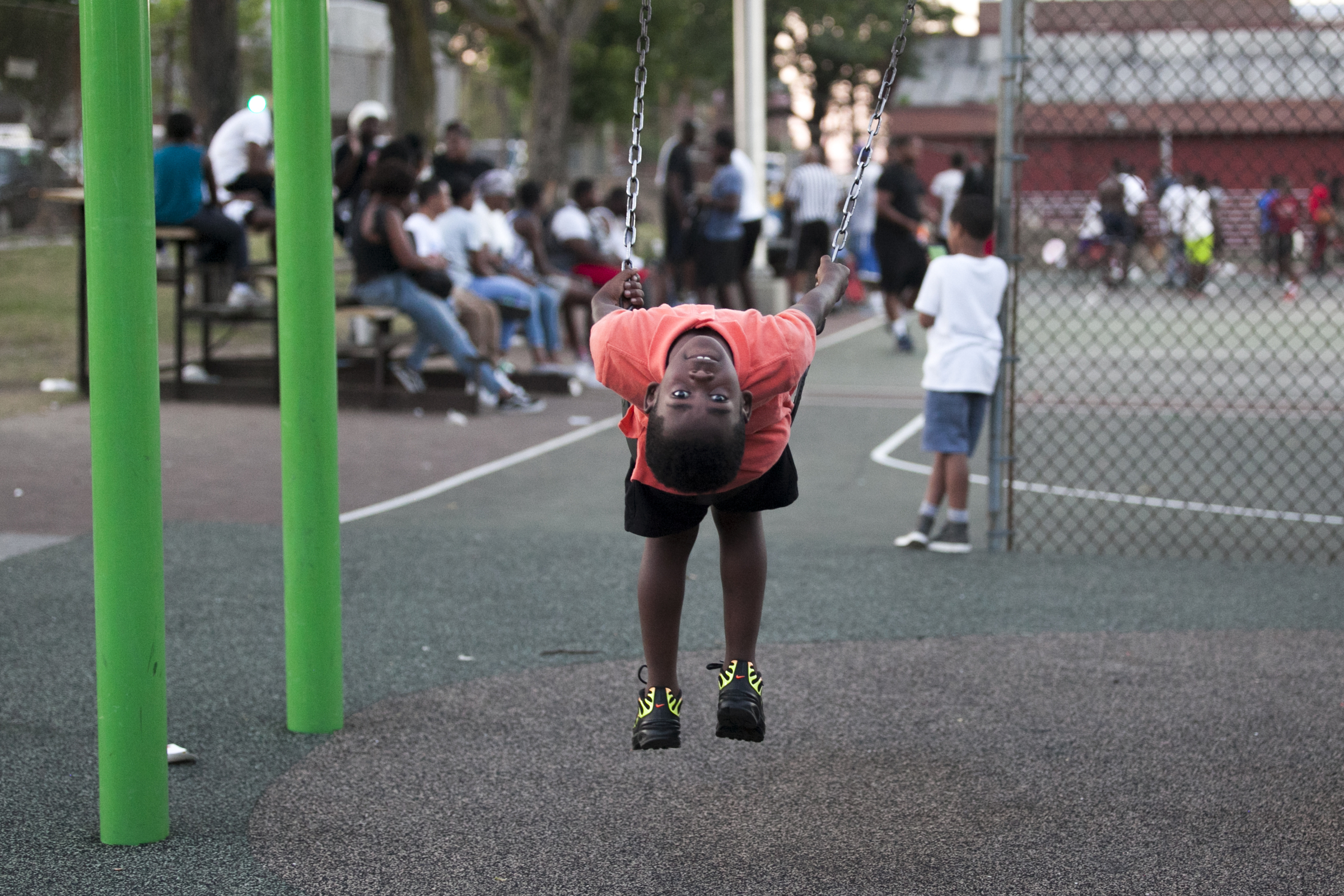 A young Philadelphia looks backwards from his swing at Dendy Playground on the evening of Wednesday, July 18, 2018. | Maggie Loesch for PlanPhilly