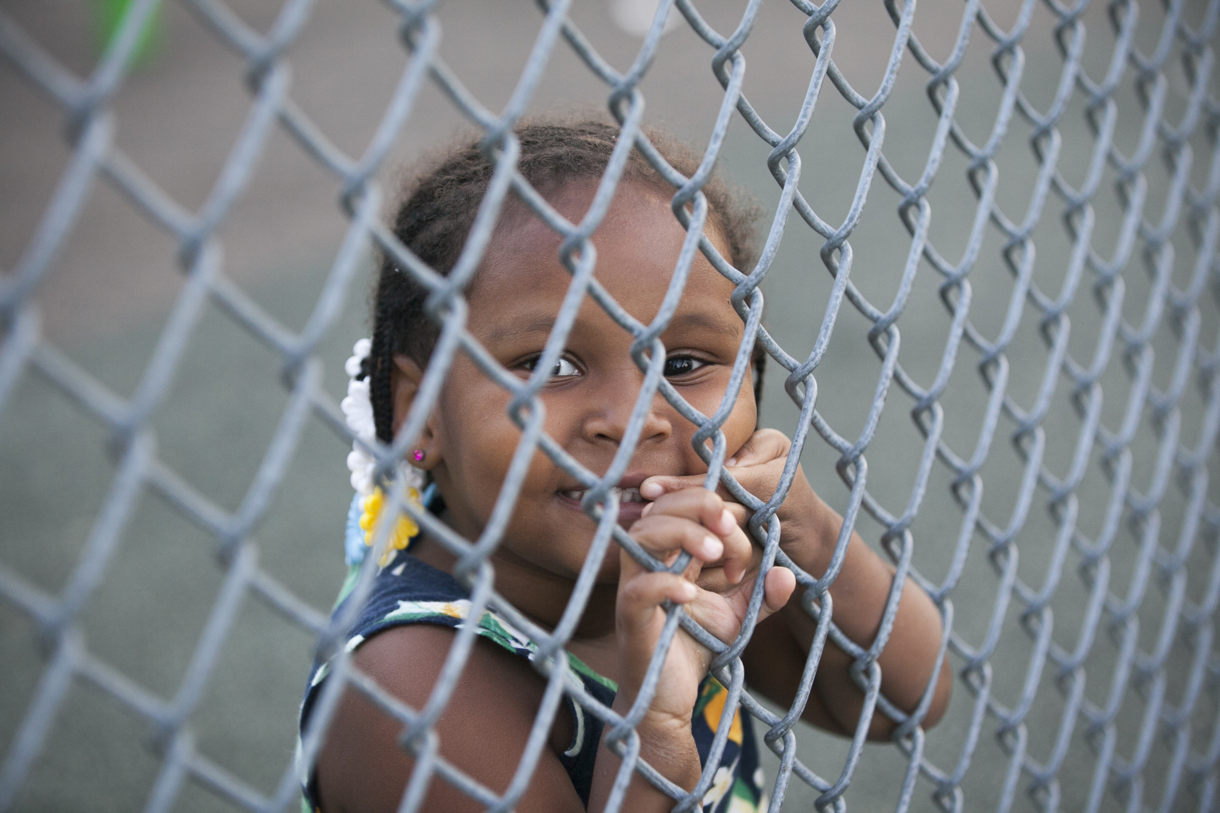 Mimi, 2, peers through the fence separating basketball courts from the play equipment at Dendy. | Maggie Loesch 