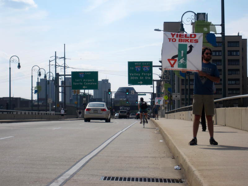 Ambassador Julian Root holds up a sign on the Walnut Street Bridge urging cars to yield to bikes.
