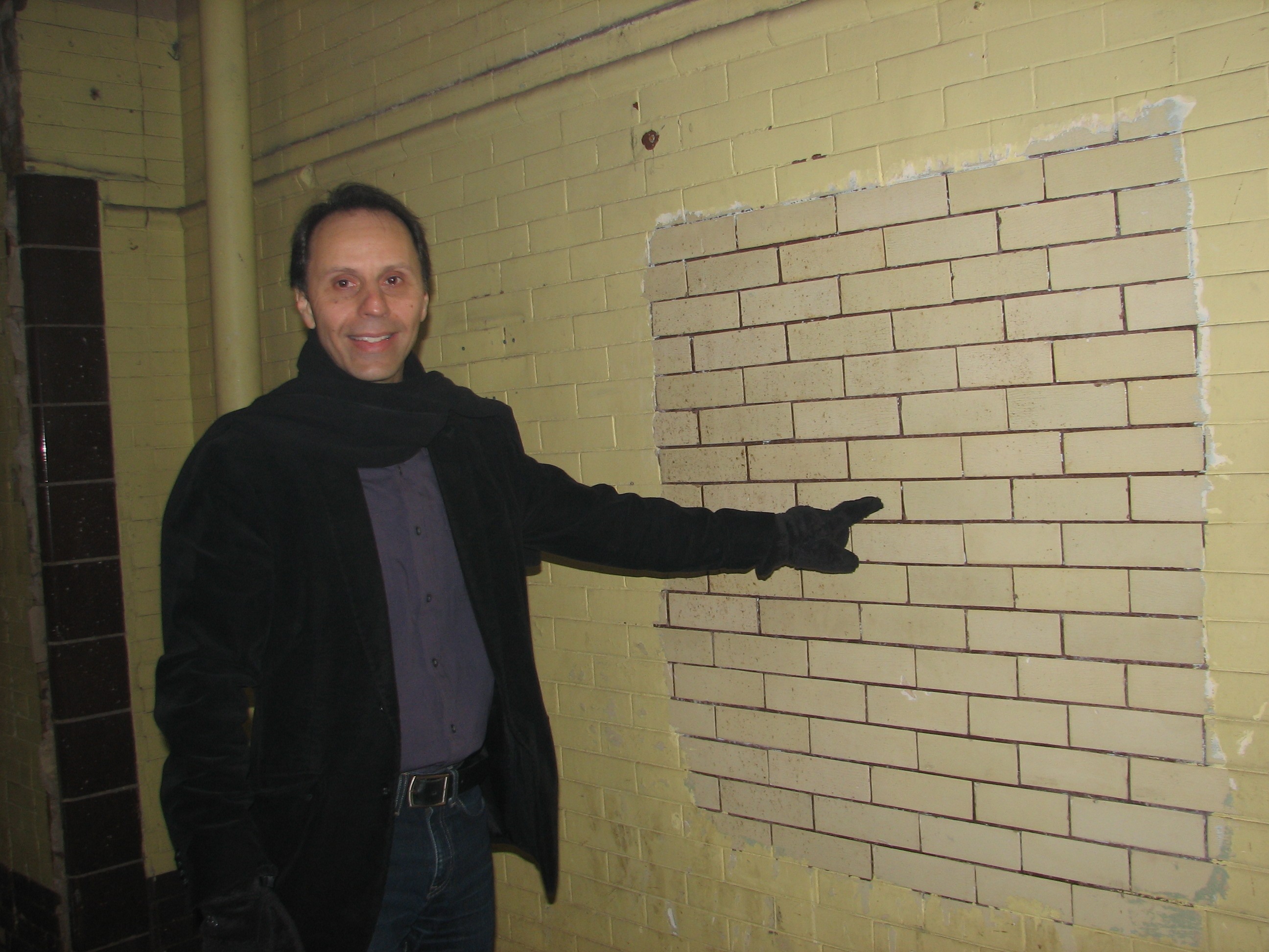 Philly Fringe President Nick Stuccio points out what lies on the walls of the building beneath a layer of paint: Original glazed brick. The construction dust makes it hard to see the color. They are a pale yellow.