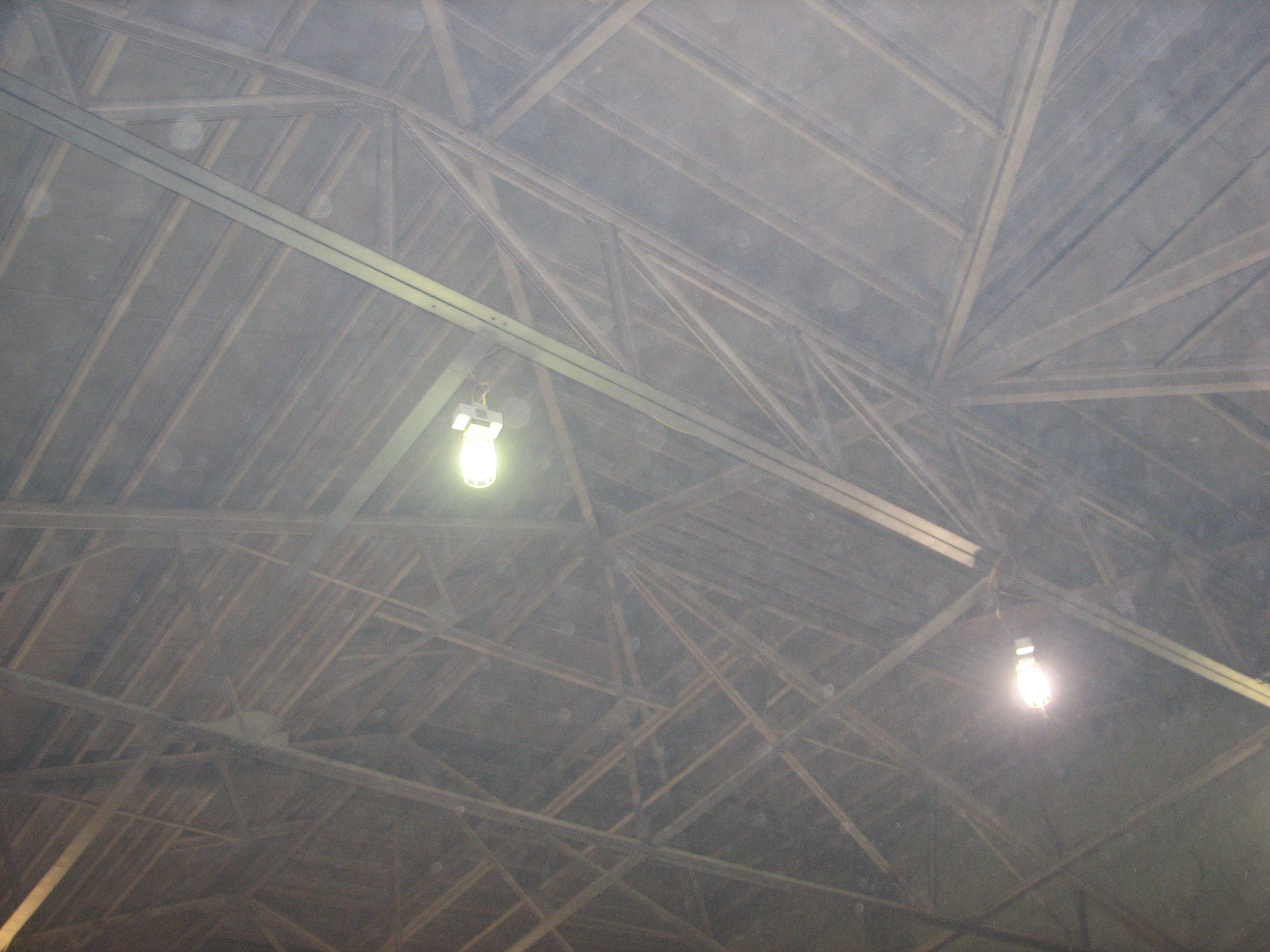 The intricate trusswork of the roof can be seen through a thick layer of construction dust.