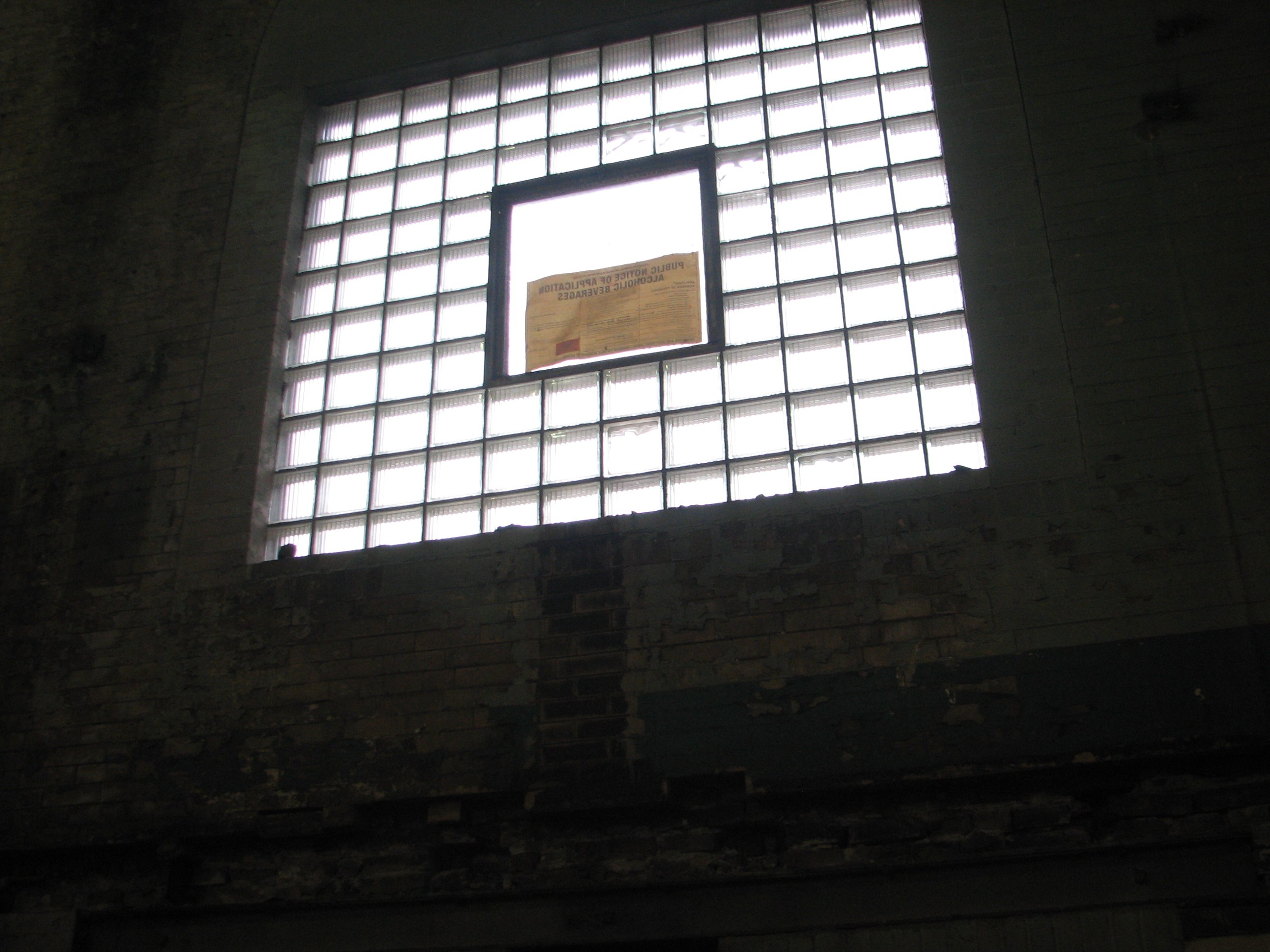 One of many large windows at the old pumping station. The glass block will be removed, along with brickwork, to restore the windows to their original size.  A liquor license application is visible in the window. Stuccio said the ability to have a bar/restaurant social space was part of the decision to buy this building.