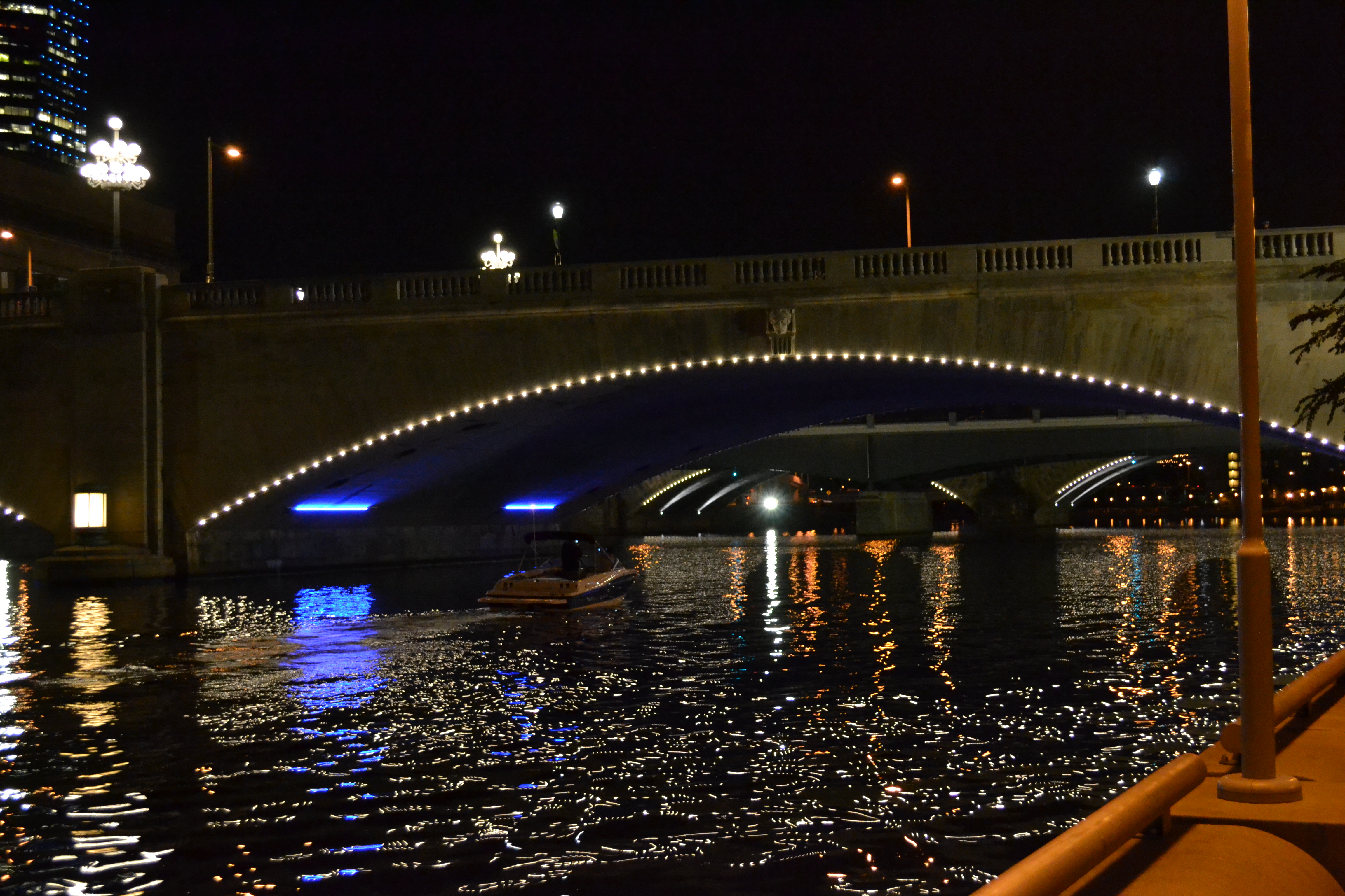 A boat cruised beneath the illuminated bridges as the lights danced on the water